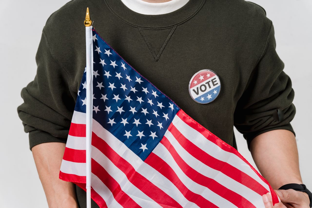 services-01 A person holding an American flag with a vote badge, symbolizing patriotism and democracy.